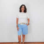 Woman wearing a white t-shirt and light blue shorts standing against a plain white wall.