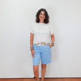 Woman wearing a white t-shirt and light blue shorts standing against a plain white wall.