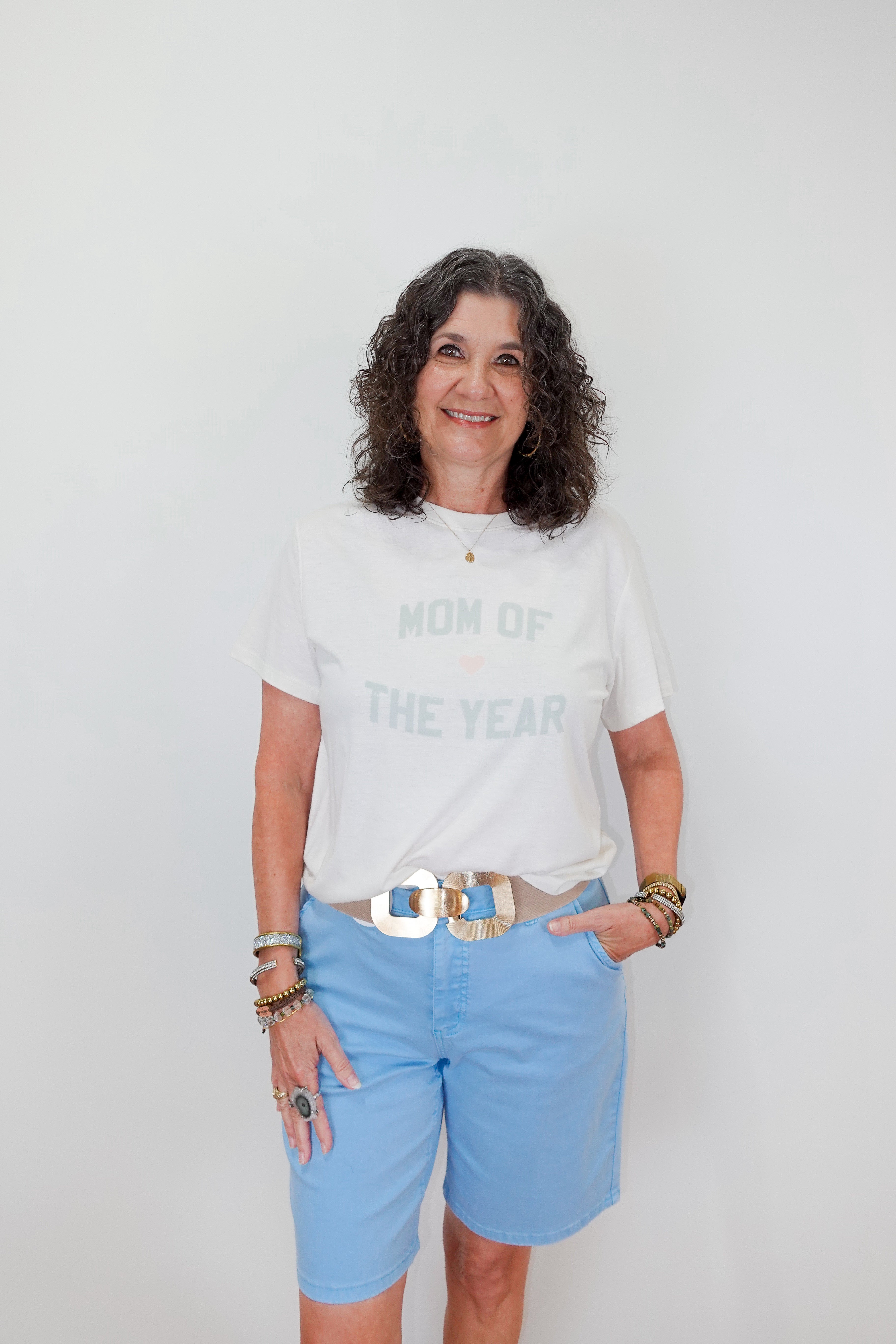 Woman wearing a white t-shirt with text and light blue shorts against a plain background