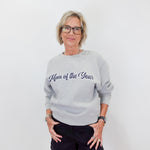 Woman wearing a gray sweatshirt with 'Mom of the Year' text on a white background
