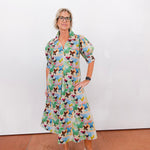 Woman wearing a colorful butterfly-patterned dress against a white wall.
