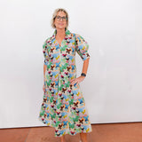 Woman wearing a colorful butterfly-patterned dress against a white wall.