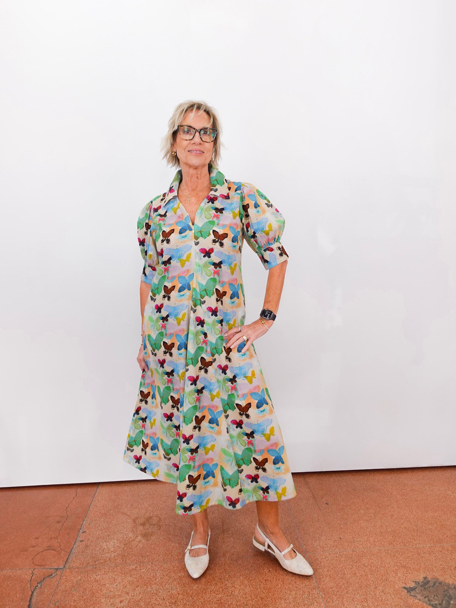 Woman wearing a colorful butterfly-patterned dress against a white wall.