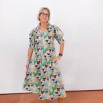 Woman wearing a colorful butterfly-patterned dress against a white wall.