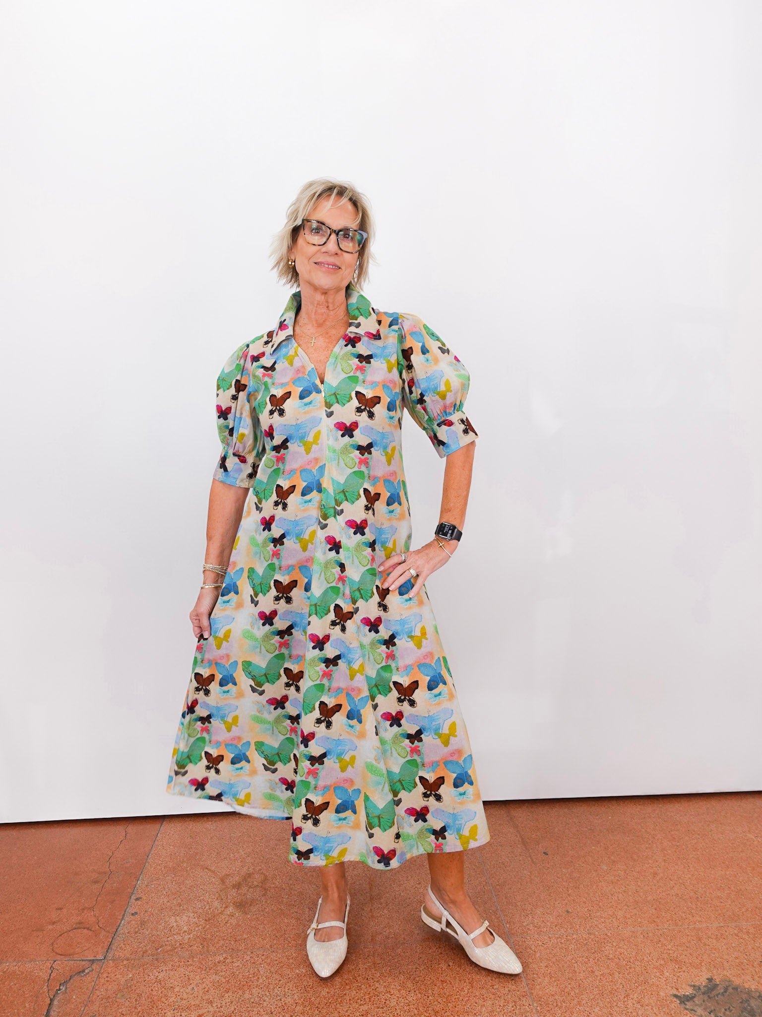 Woman wearing a colorful butterfly-patterned dress against a white wall.