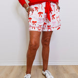 Person wearing a red sweater, white shorts with red patterns, and white sneakers against a plain background