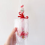 Hand holding a clear plastic bag with colorful text and a red ribbon against a white background