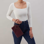 Person wearing a white long-sleeve top and blue jeans holding a maroon handbag against a gray background