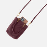 Maroon handbag with braided handle and gold chain, containing a phone, on a light gray background