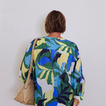 Person wearing a colorful leaf-patterned shirt against a white wall