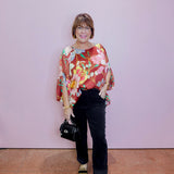 Woman wearing a colorful floral blouse and black pants against a plain background