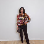 Woman wearing a patterned shirt and black pants against a white wall.