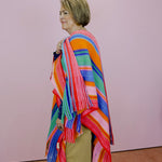 Person wearing a colorful striped shawl against a plain background
