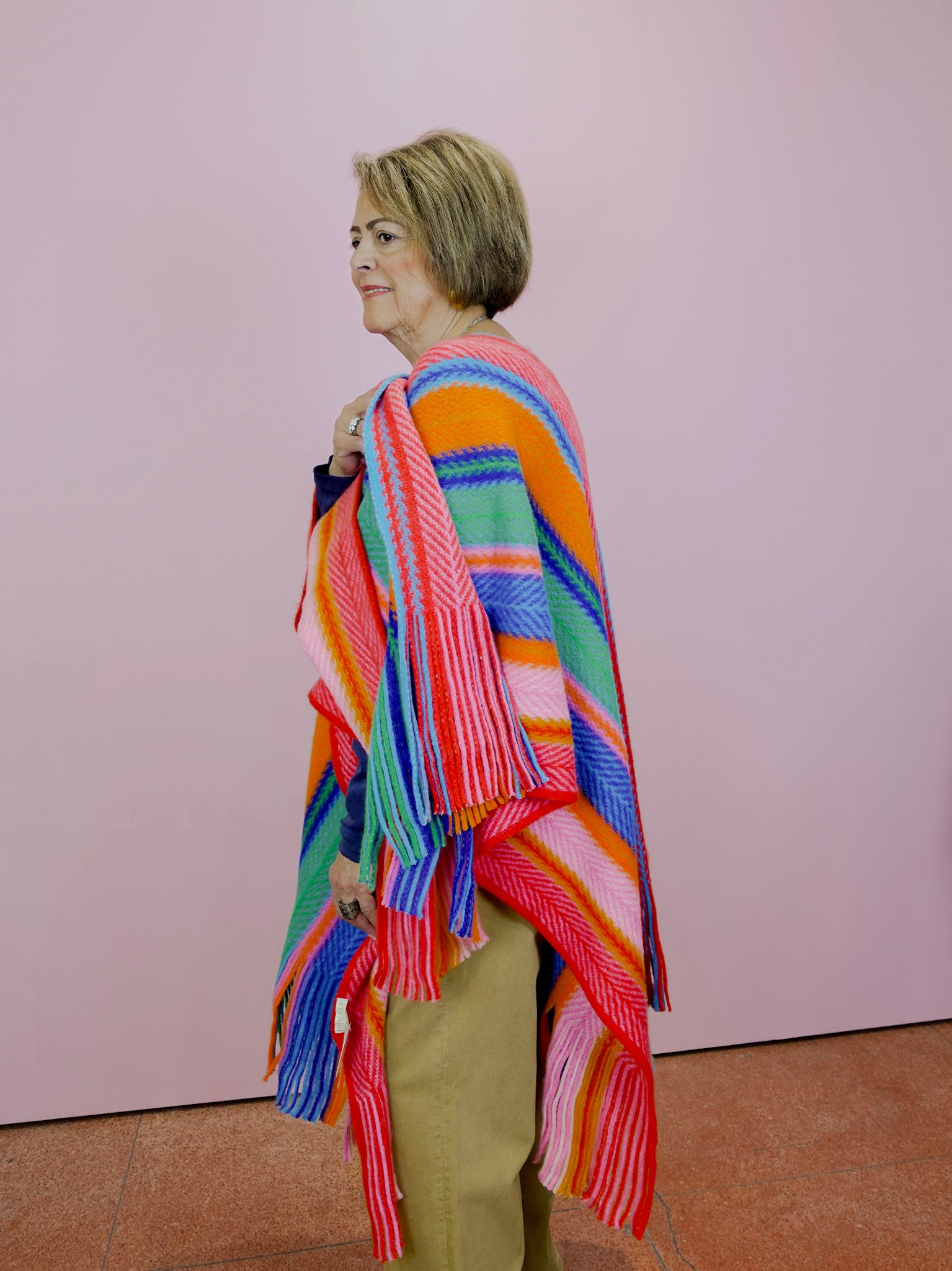 Person wearing a colorful striped shawl against a plain background