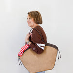 Woman holding a large woven bag against a plain background