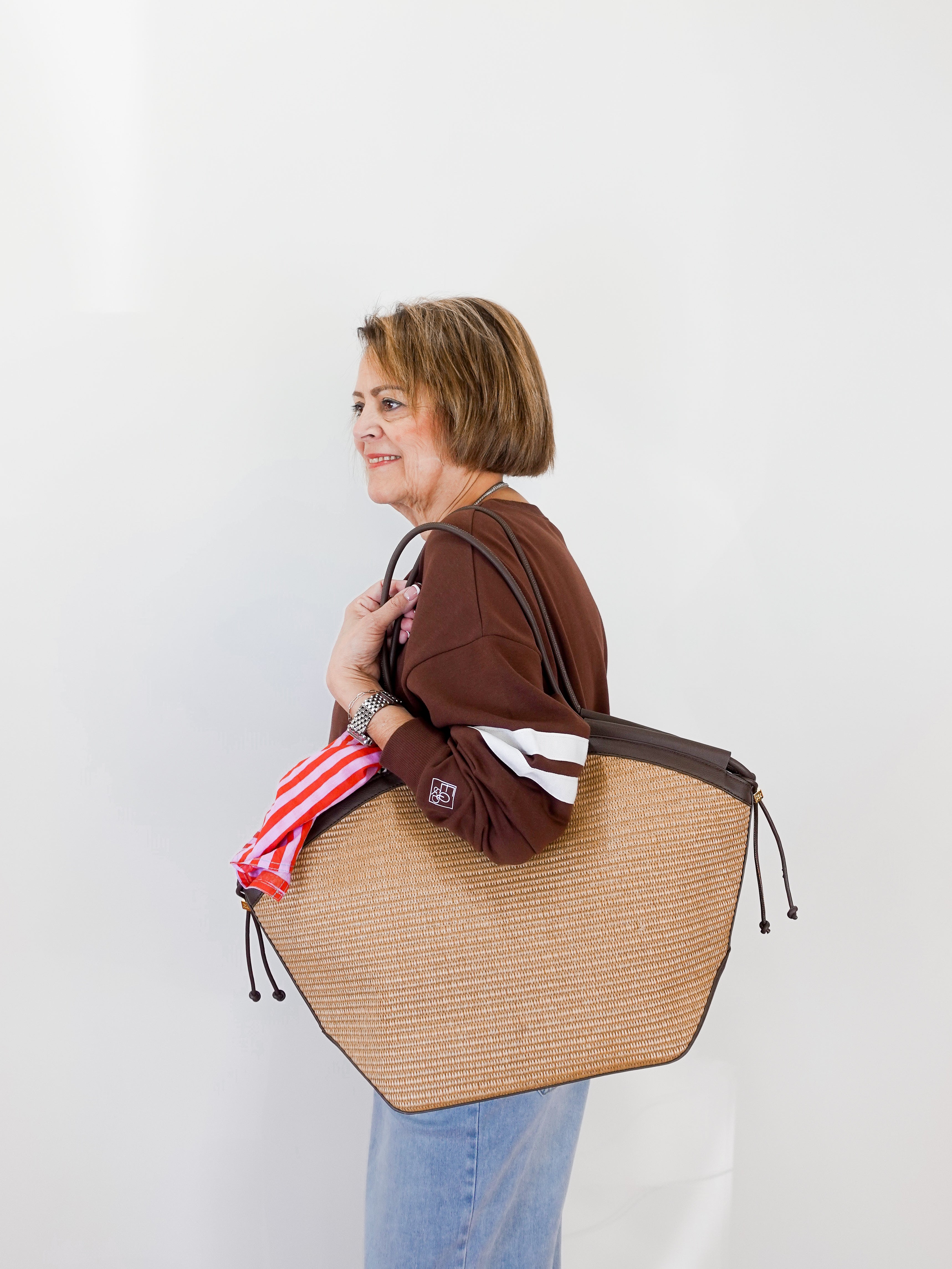 Woman holding a large woven bag against a plain background