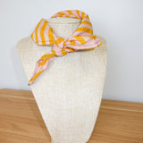 Mannequin head with a yellow and pink striped scarf on a wooden surface.