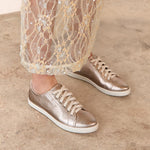 Bronze sneakers worn with sheer lace pants on a neutral background