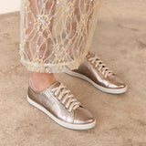 Bronze sneakers worn with sheer lace pants on a neutral background