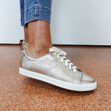 Silver sneaker worn with blue jeans on a brown floor.