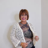 Woman wearing a white lace cardigan over a patterned top against a plain background