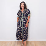 Woman wearing a floral dress standing against a white wall.