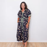 Woman wearing a floral dress standing against a white wall.