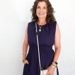 Woman wearing a navy dress with a white handbag against a plain background