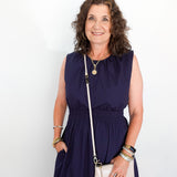 Woman wearing a navy dress with a white handbag against a plain background