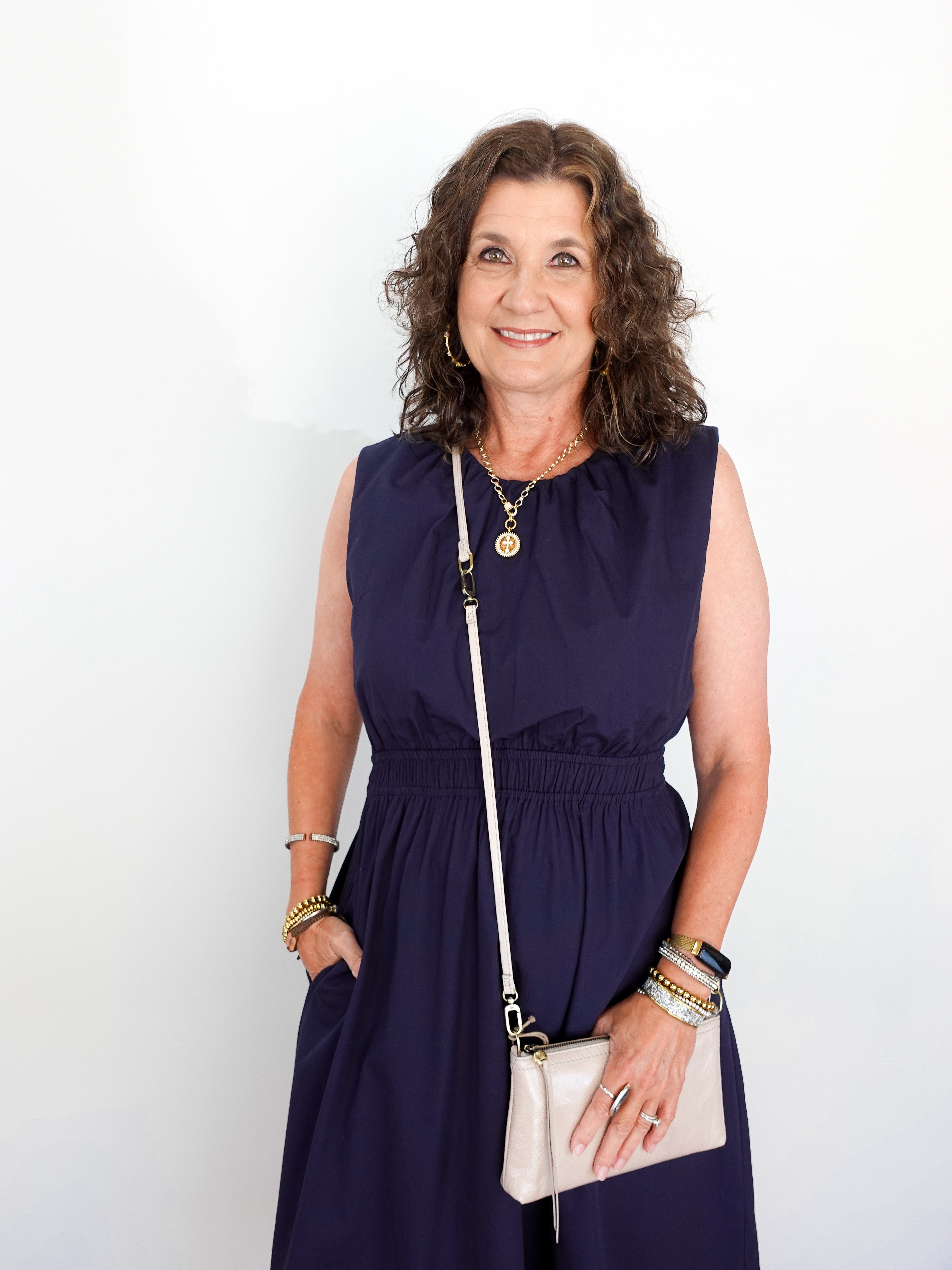 Woman wearing a navy dress with a white handbag against a plain background