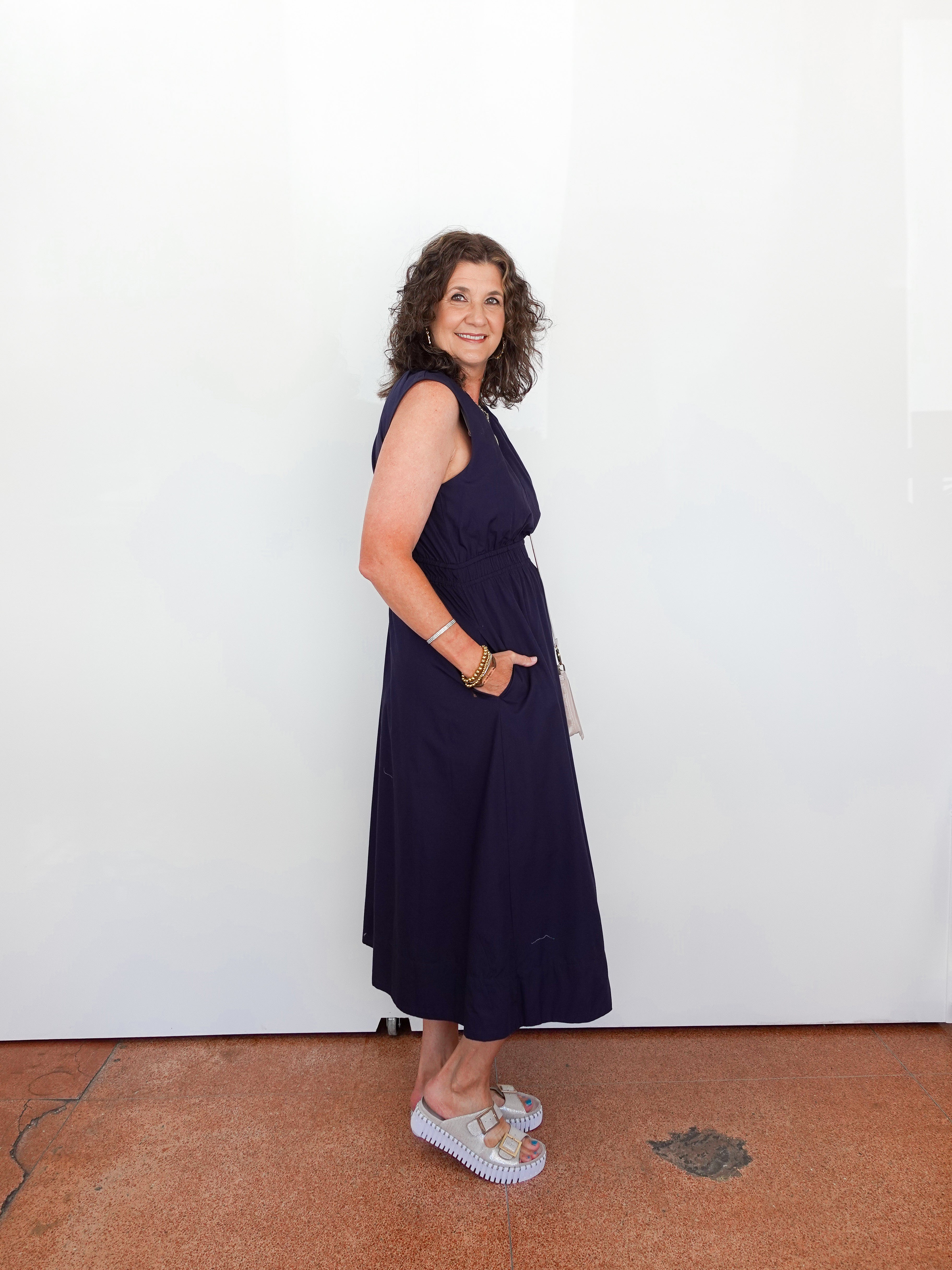 Woman wearing a navy blue dress standing against a white wall.