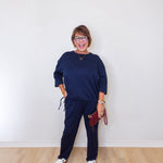 Woman wearing a navy blue outfit with white sneakers against a white wall.