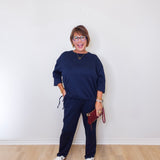 Woman wearing a navy blue outfit with white sneakers against a white wall.