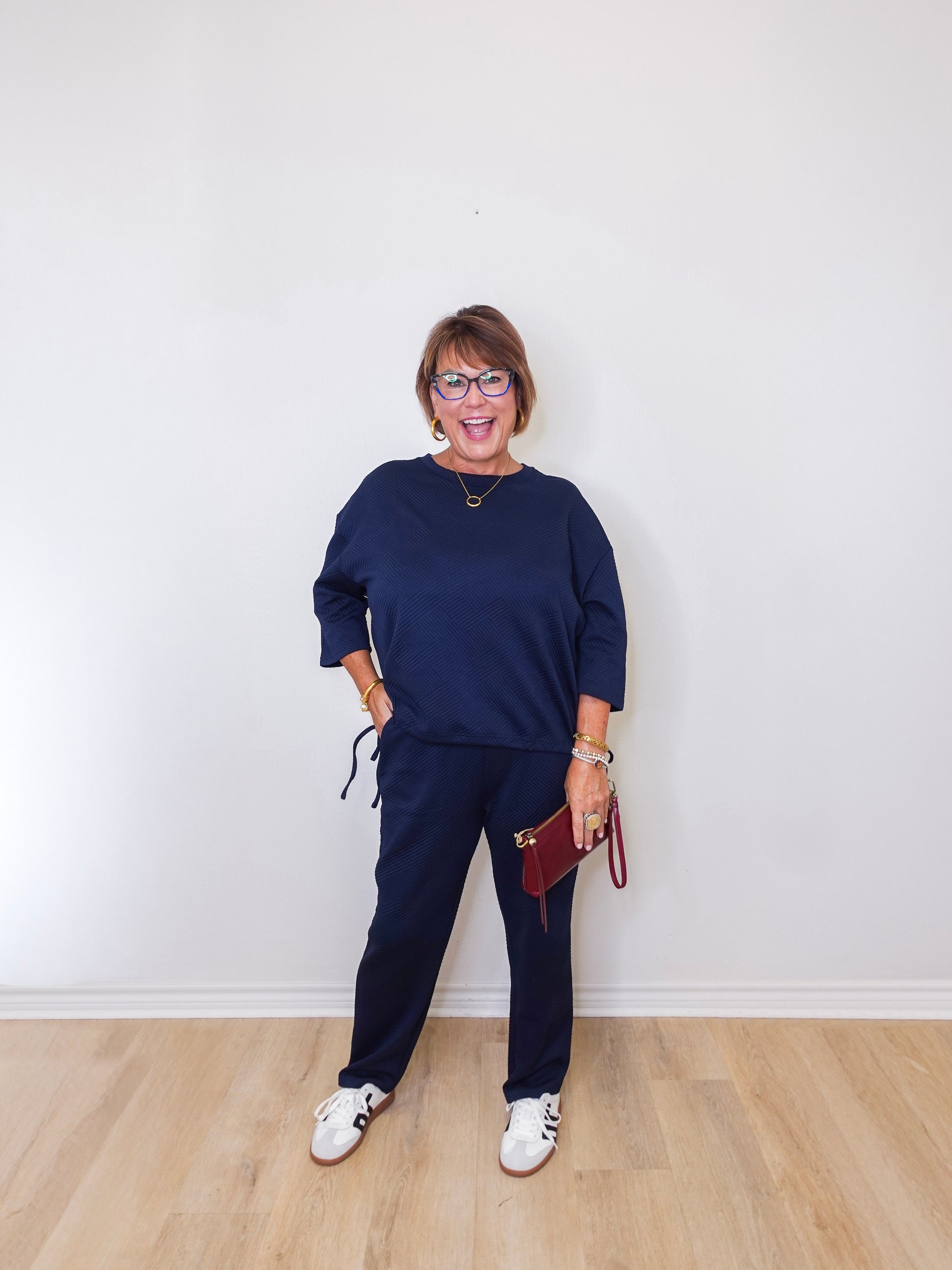 Woman wearing a navy blue outfit with white sneakers against a white wall.