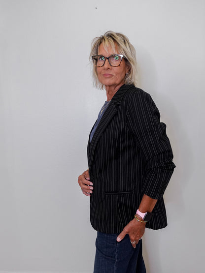 Person wearing a black pinstripe blazer against a plain background