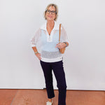 Woman wearing a white crochet top and dark pants against a plain background