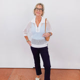 Woman wearing a white crochet top and dark pants against a plain background