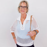 Woman wearing a white mesh top with a plain background