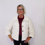 Person wearing a white jacket over a red shirt with a plain background