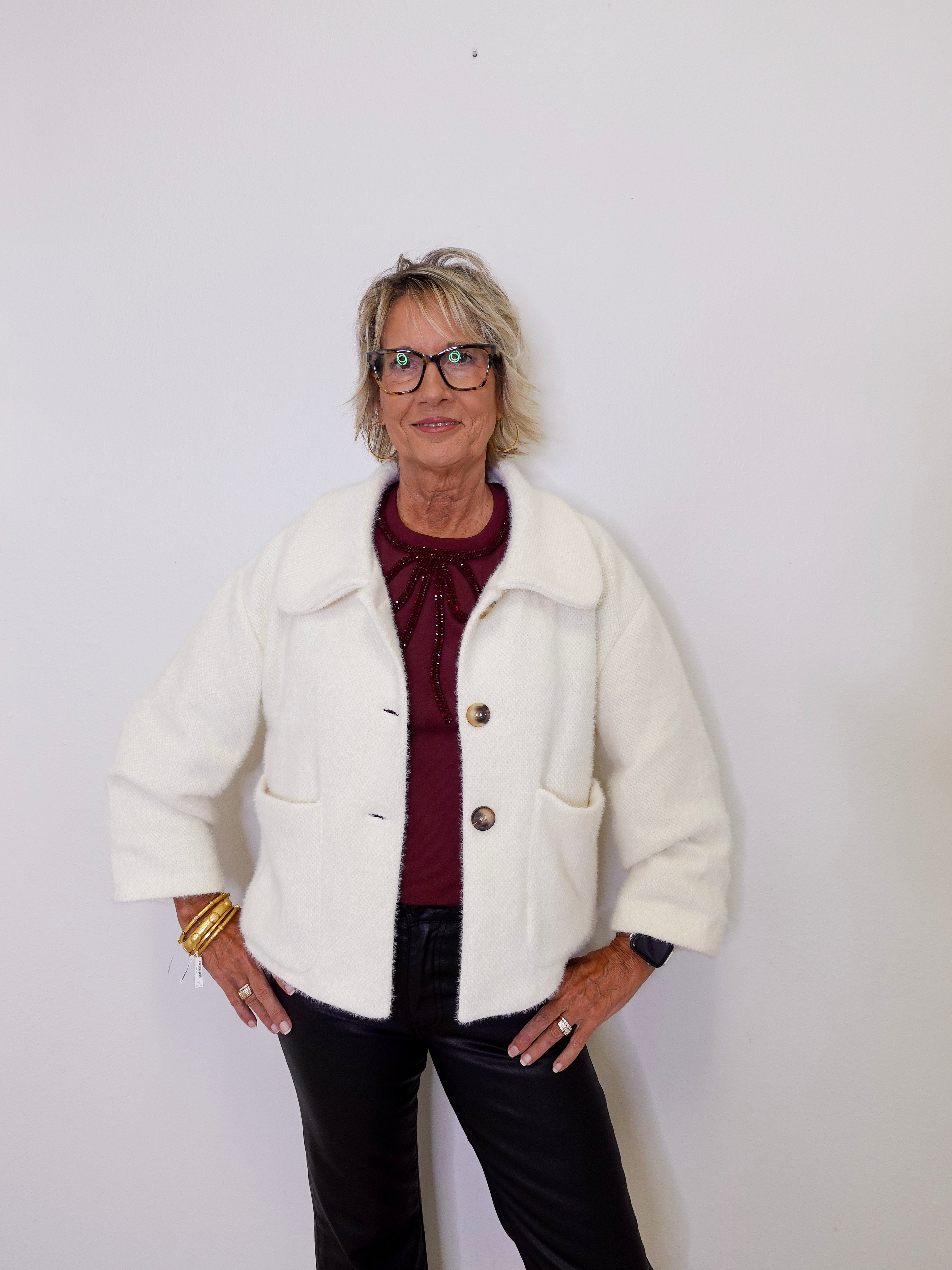 Person wearing a white jacket over a red shirt with a plain background