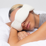 Person lying down with a white eye mask on a plain background