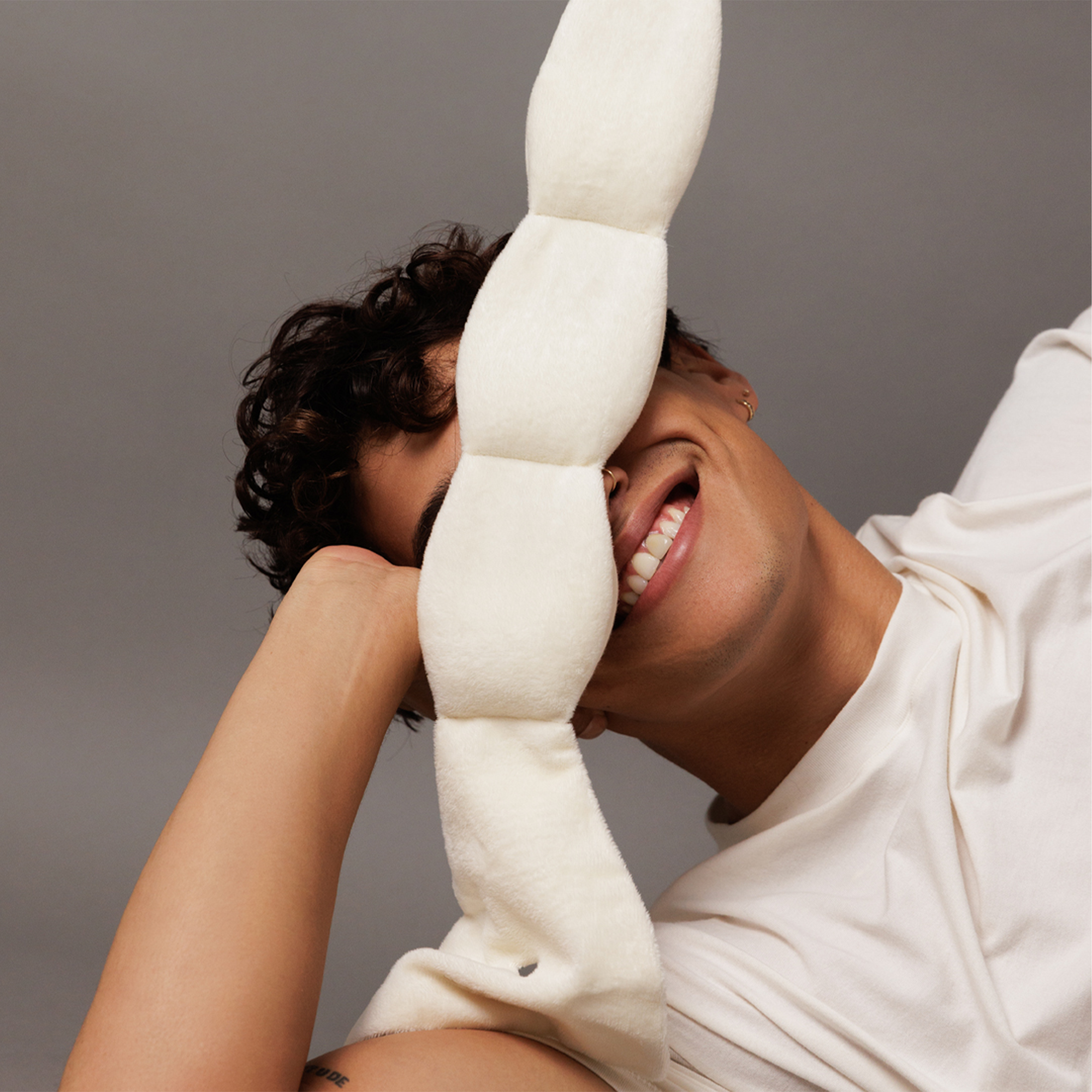 Person holding a large white plush toy against a gray background
