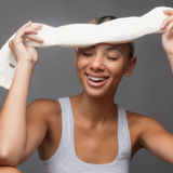 Woman stretching a white rubber band above her head against a gray background