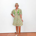 Woman wearing a floral dress standing against a white wall.