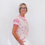 Woman wearing a pink floral blouse and white pants against a plain background