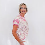 Woman wearing a pink floral blouse and white pants against a plain background