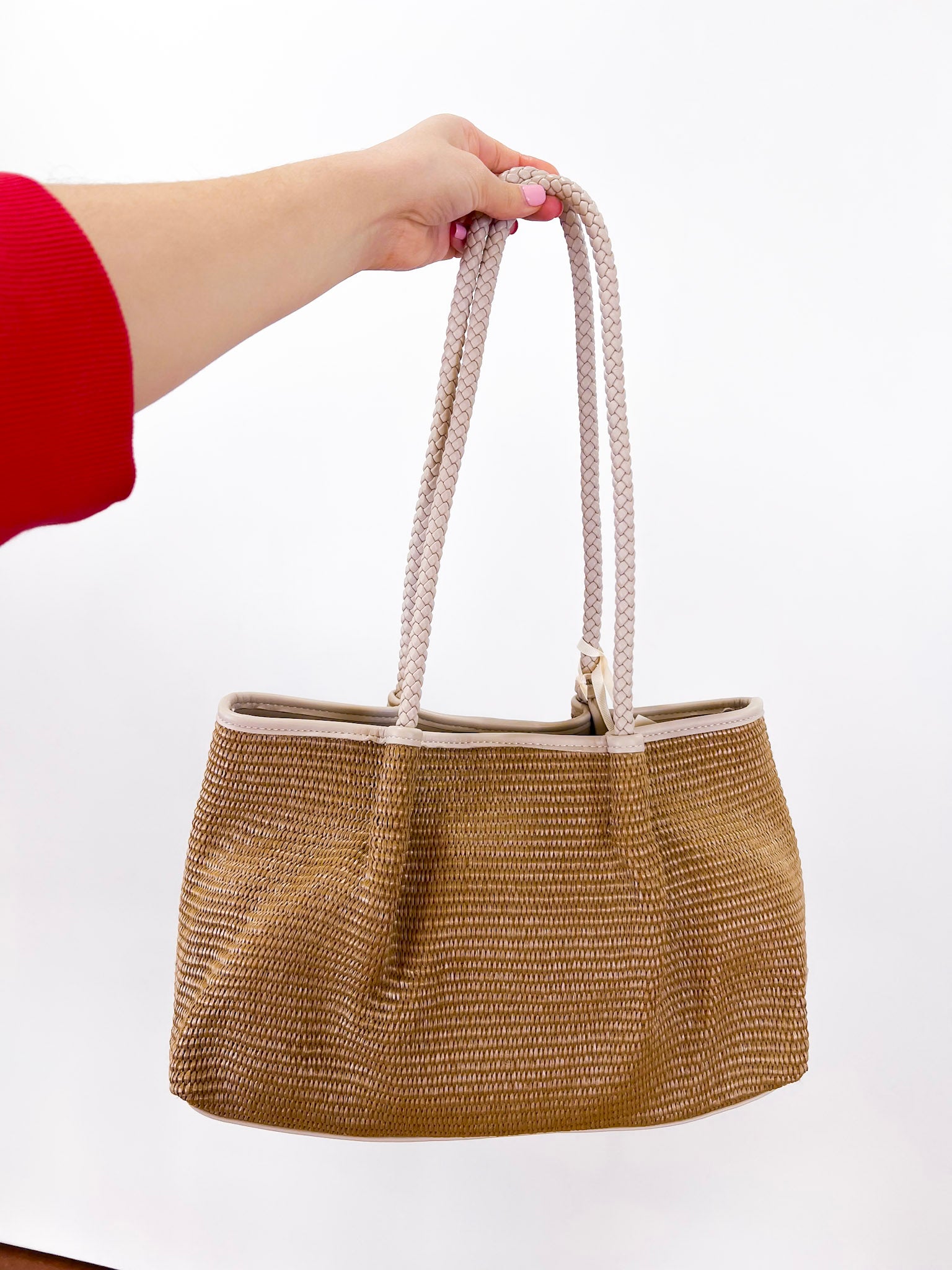 Hand holding a woven handbag against a white background