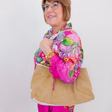 Woman wearing a colorful floral jacket and holding a straw bag against a white background