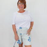 Woman wearing a white top and floral shorts with a blue handbag against a white background