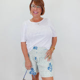Woman wearing a white top and floral shorts with a blue handbag against a white background